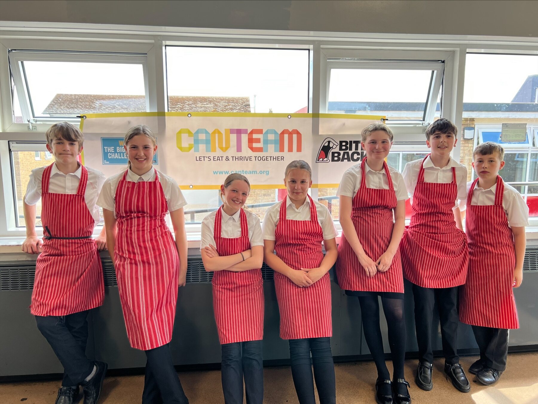 Secondary-aged CanTeam Crew members wearing red striped aprons in front of a CanTeam banner